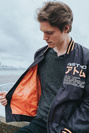 Black Nylon Astroboy Bomber jacket in black and orange. Has a zipper with an orange tag on the left sleeve with Astroboy written on one side and Bibisama on the other. Has Astroboy x Bibisama patch on the right sleeve. On the left chest, Astroboy is written on top with information on manufacturer and designer.